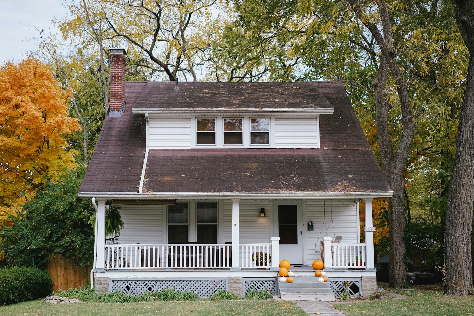 Bungalow with wraparound porch, autumn foliage, pumpkins on steps